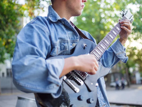 Genç adam şarkı söylüyor ve doğal bir arka plan üzerinde bir parkta bir kot ceket gitar çalar. Müzik konsepti.