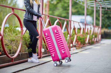 Bir kız pembe bavulla korkuluk tarafından duruyor