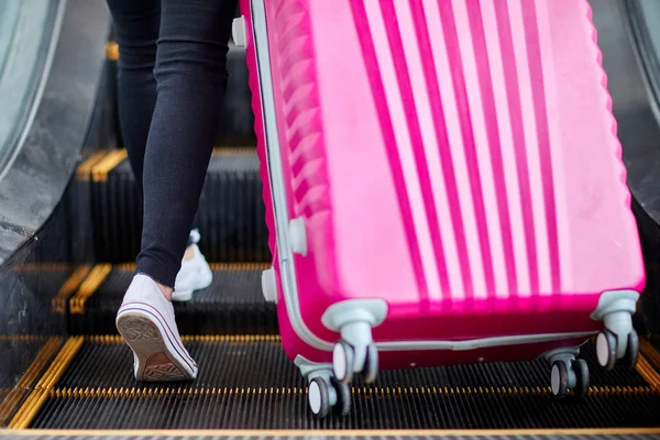 Das Mädchen hebt einen rosafarbenen Koffer auf die Rolltreppe — Stockfoto