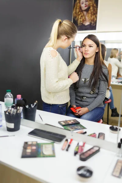 Um maquiador está aplicando maquiagem a uma jovem . — Fotografia de Stock