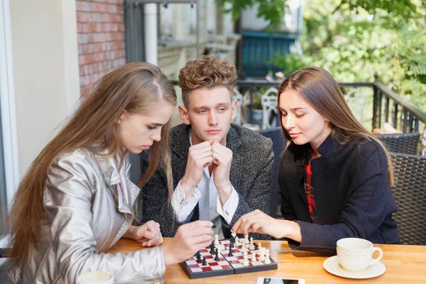 Красивий хлопець і розумна дівчина друзі грають в шахи на фоні кафе. Концепція інтелектуальних ігор . — стокове фото