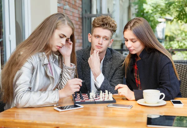 Chico guapo y amigas inteligentes jugando al ajedrez en un fondo de café. Concepto juegos de inteligencia . — Foto de Stock