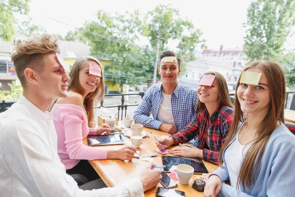 Друзі-підлітки розважаються, граючи з наклейками на чолах на фоні кафе. Концепція діяльності друзів . — стокове фото