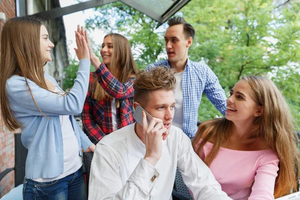 Yakışıklı adam bir telefon arıyor. Bir mobil kafe arka plan üzerinde heyecanlı gençler grup. Yeni smartphone kavramı.