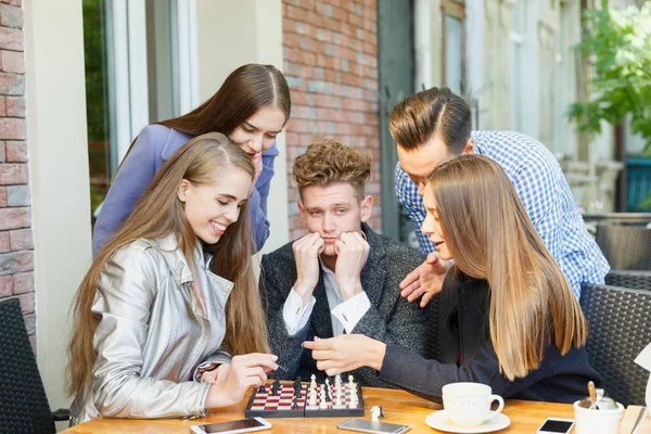 Jóvenes amigos reflexivos que tienen una competencia de ajedrez en un fondo de café. Concepto de amistad . — Foto de Stock