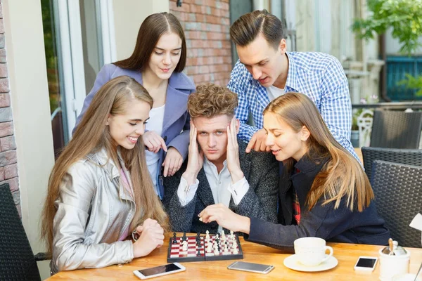 Jeugdvrienden spelen een schaakspel en denken op de achtergrond van een café. Schaken spelen concept. — Stockfoto