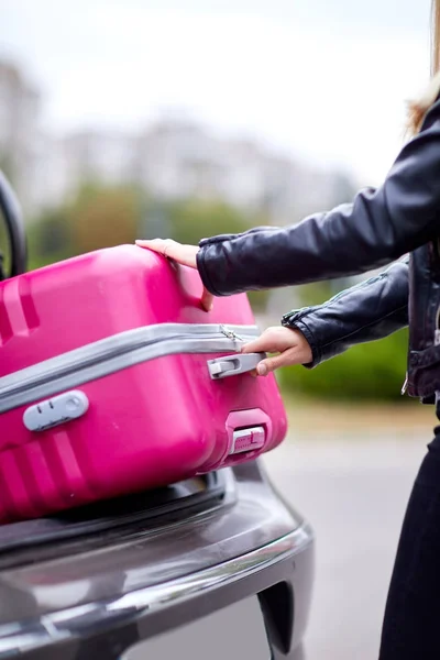 Das Mädchen holt ihren rosa Koffer aus dem Kofferraum — Stockfoto