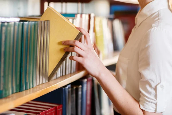 Женская рука выбирает книгу в библиотеке . — стоковое фото