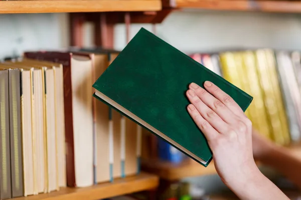 En kvinnas hand väljer en bok i biblioteket. — Stockfoto