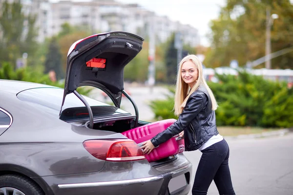 A lány veszi ki neki rózsaszín bőröndöt a csomagtartóba — Stock Fotó