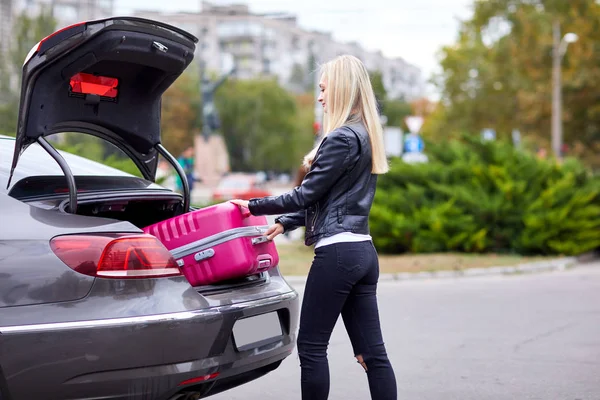 A lány veszi ki neki rózsaszín bőröndöt a csomagtartóba — Stock Fotó