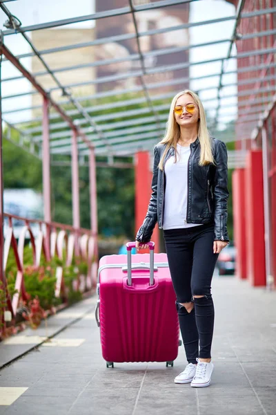 Blondes Mädchen steht mit rosa Koffer am Bahnhof — Stockfoto