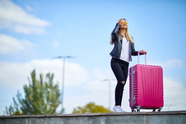 Mädchen mit einem rosa Koffer auf einem Hintergrund von einem schönen blauen Himmel — Stockfoto