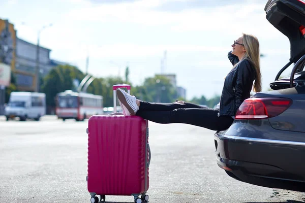 Mädchen auf dem Hintergrund eines offenen Kofferraums mit einem rosa Koffer — Stockfoto