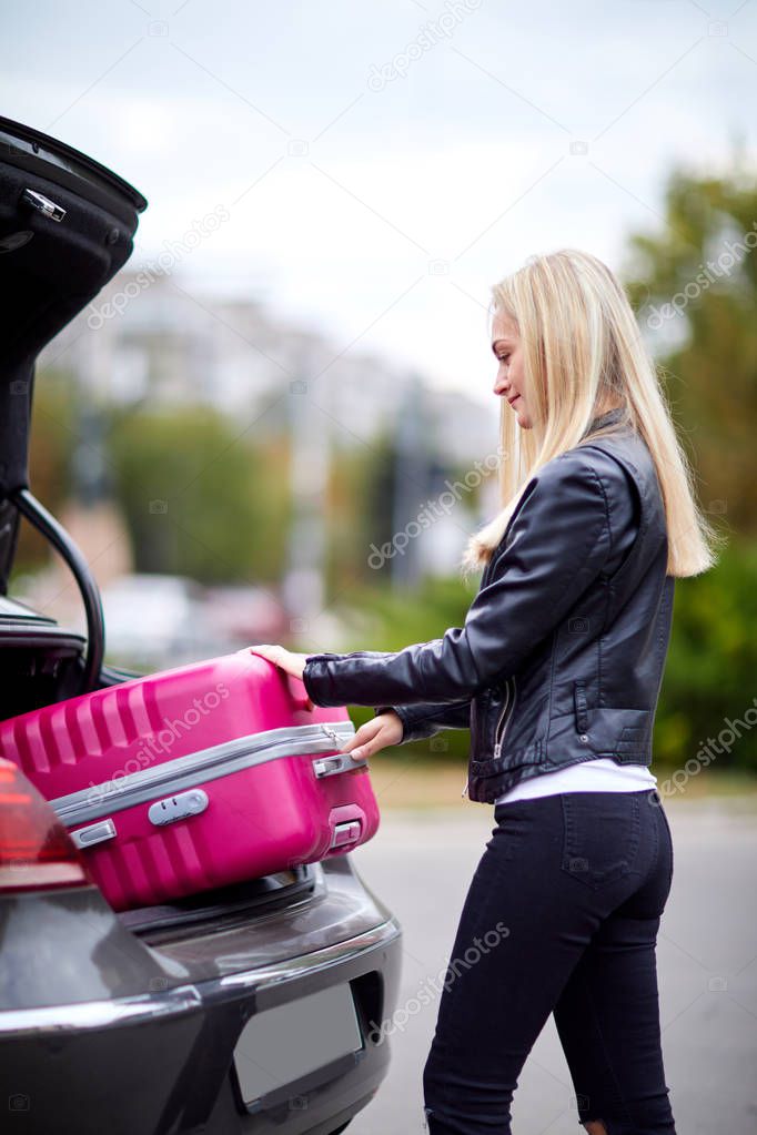 The girl takes out her pink suitcase from the trunk
