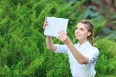 Bir tablet ile bir parkta genç esmer kız oturuyor.