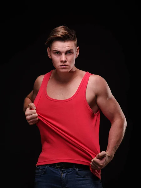 Gezonde, mooie, jonge man, zijn rode t-shirt te trekken op een zwarte achtergrond. Sportieve levensstijl concept. — Stockfoto