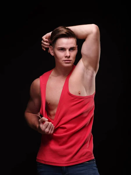 Healthy, beautiful, young man pulling his red t-shirt on a black background. Sporty lifestyle concept. — Stock Photo, Image