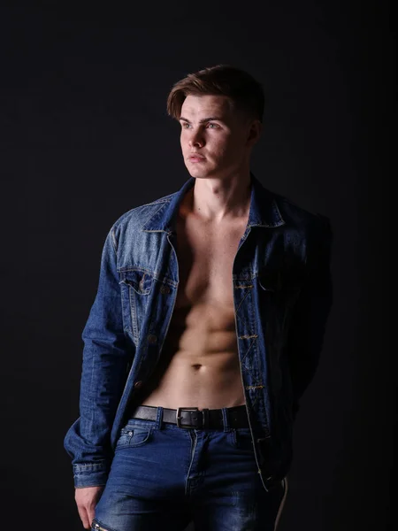Un ragazzo alla moda con una giacca di jeans su sfondo nero. Sexy bell'uomo elegante. Concetto moda moderna . — Foto Stock