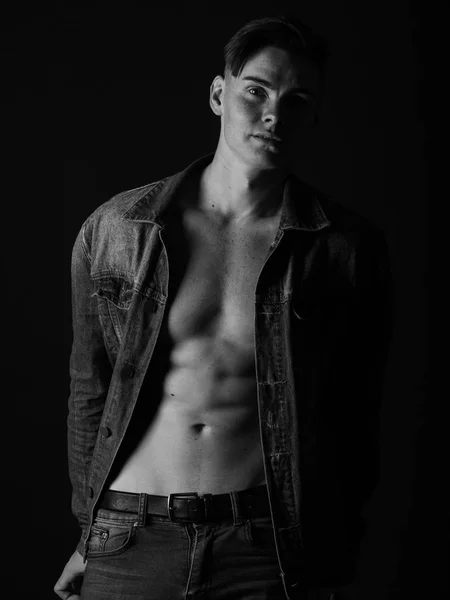 Homem ajuste lindo em uma jaqueta de jeans, sem camisa em um fundo preto. preto e branco sexy homem conceito . — Fotografia de Stock