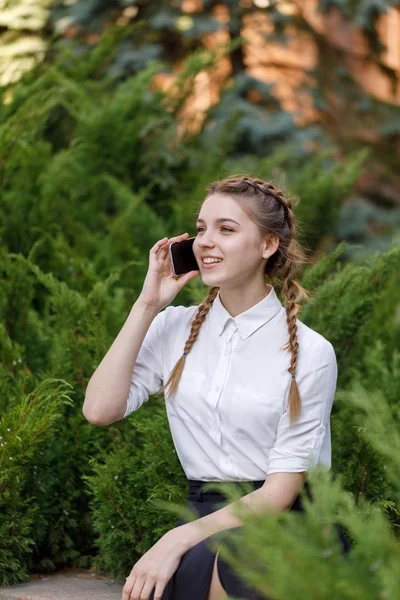 Genç mutlu kadın şehir parkında oturan cep telefonu üzerinde söz.