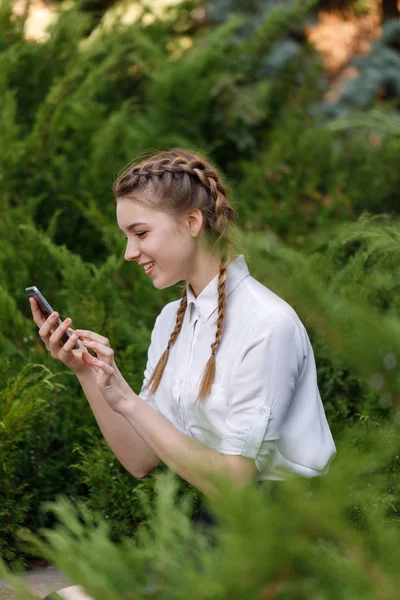 Gelukkig jong meisje in park met telefoon in handen. — Stockfoto