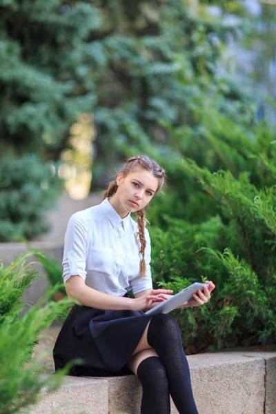 Młoda brunetka dziewczyna siedzi w parku z tabletem. — Zdjęcie stockowe