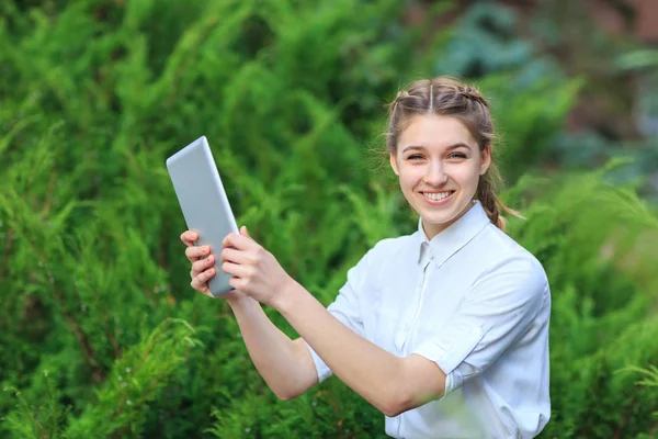 Bir tablet ile bir parkta genç esmer kız oturuyor.