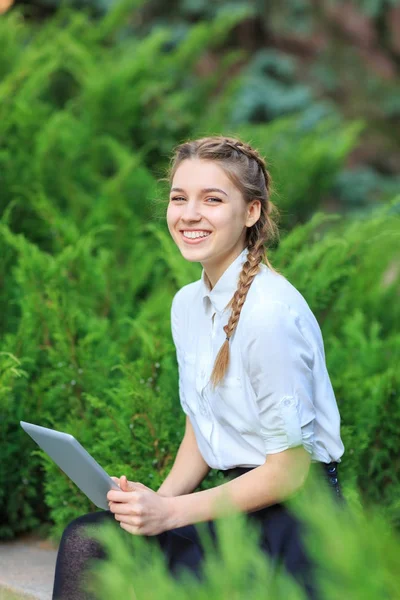 Bir tablet ile bir parkta genç esmer kız oturuyor.
