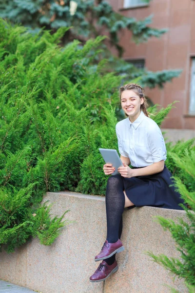 Uma jovem morena senta-se em um parque com um tablet . — Fotografia de Stock