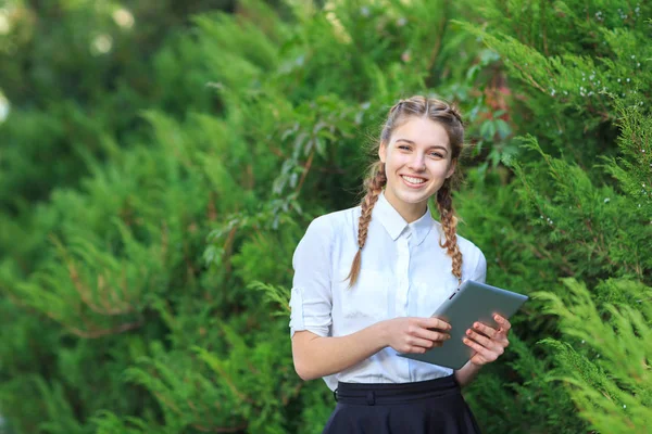 Une jeune fille brune s'assoit dans un parc avec une tablette . — Photo