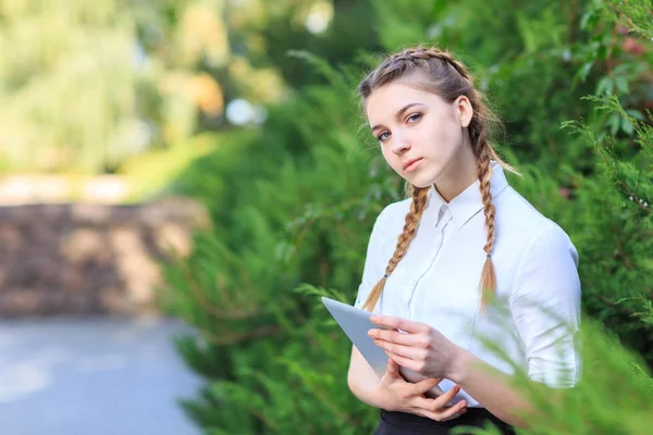 Een jonge brunette meisje zit in een park met een tablet. — Stockfoto