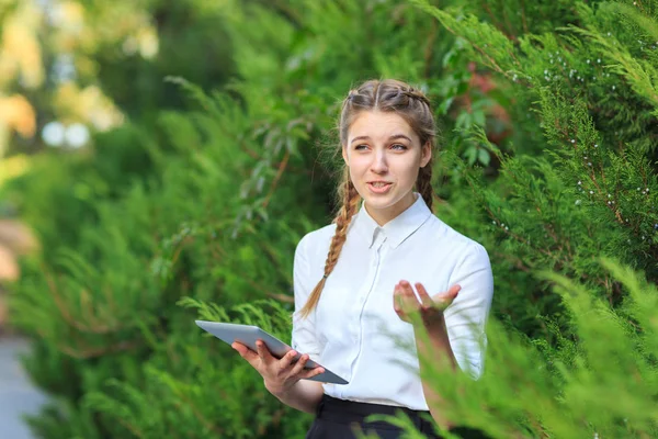 Bir tablet ile bir parkta genç esmer kız oturuyor.