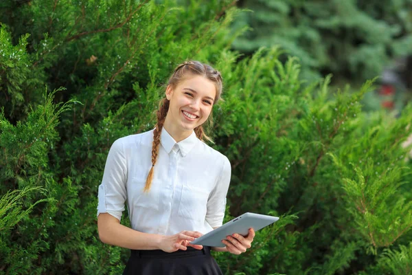 Bir tablet ile bir parkta genç esmer kız oturuyor.