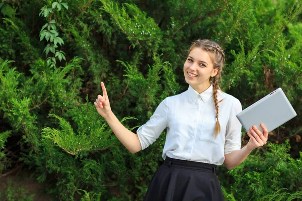 Une jeune fille brune s'assoit dans un parc avec une tablette . — Photo