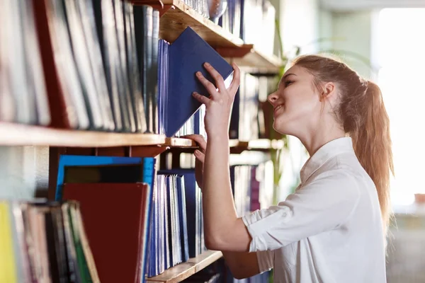 En student tar en bok från en hylla i biblioteket. — Stockfoto