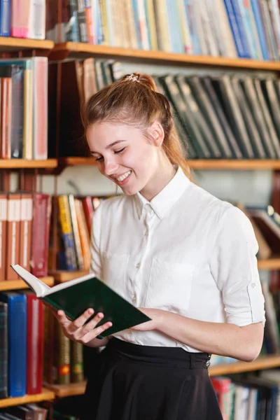 Porträtt av en ung flicka som läser en bok i biblioteket. — Stockfoto