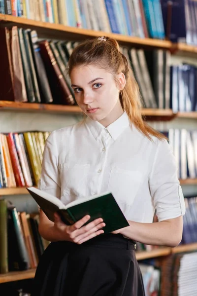Genç bir kız, bir kitapla kütüphanede portresi. — Stok fotoğraf