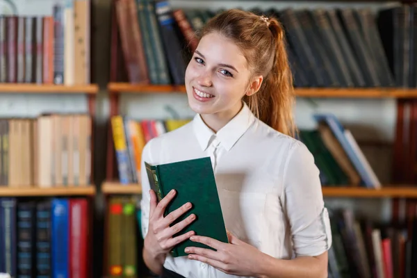 Genç bir kız, bir kitapla kütüphanede portresi. — Stok fotoğraf