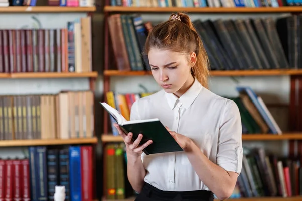 Retrato de uma jovem que está lendo um livro na biblioteca . — Fotografia de Stock
