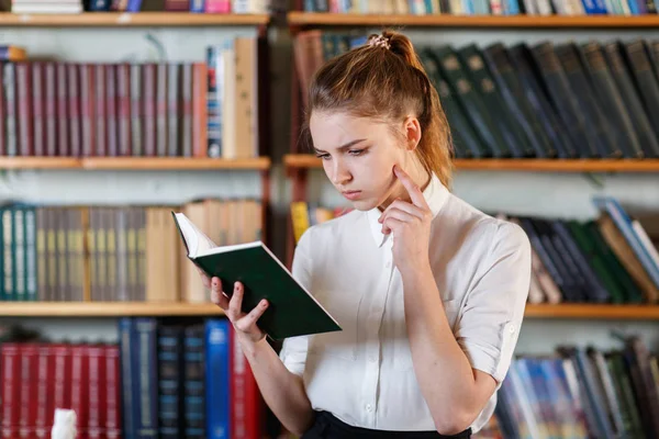 Porträtt av en ung flicka som läser en bok i biblioteket. — Stockfoto