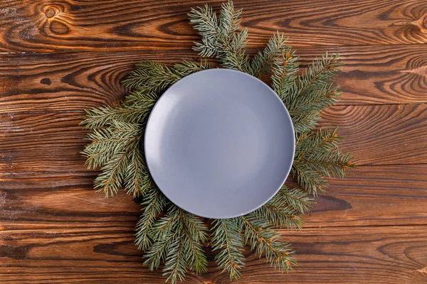 Plate empty on spruce branches on a brown background