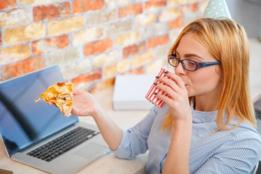 Bir dizüstü bilgisayar önünde ofiste pizza yemek bir kız