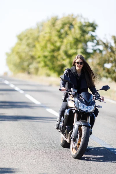 Uma menina senta-se em uma motocicleta em roupas de couro preto — Fotografia de Stock