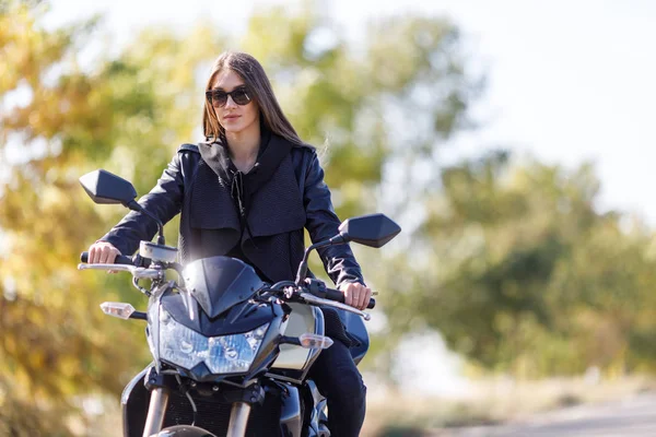 Uma menina senta-se em uma motocicleta em roupas de couro preto — Fotografia de Stock