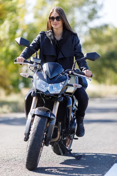 Uma menina senta-se em uma motocicleta em roupas de couro preto — Fotografia de Stock