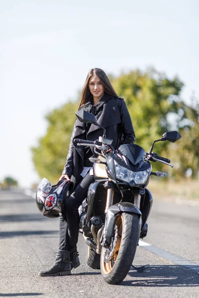 Uma menina senta-se em uma motocicleta em roupas de couro preto — Fotografia de Stock