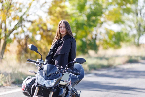 Uma menina senta-se em uma motocicleta em roupas de couro preto — Fotografia de Stock