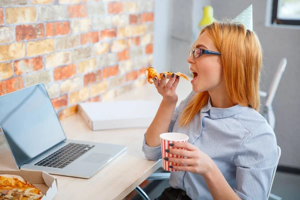 Una chica comiendo pizza en la oficina delante de un portátil —  Fotos de Stock