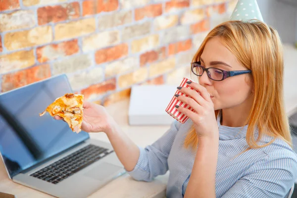 Una chica comiendo pizza en la oficina delante de un portátil —  Fotos de Stock